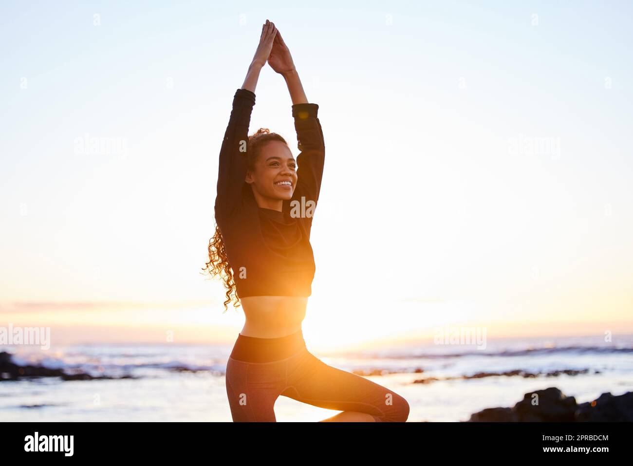 The art of yoga is balance and silence. an attractive young woman doing yoga alone on the beach at sunset. Stock Photo
