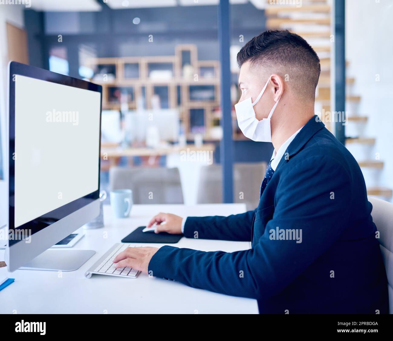 Keep it clean, some dangers go unseen. a young businessman wearing a face mask and using a computer in a modern office. Stock Photo