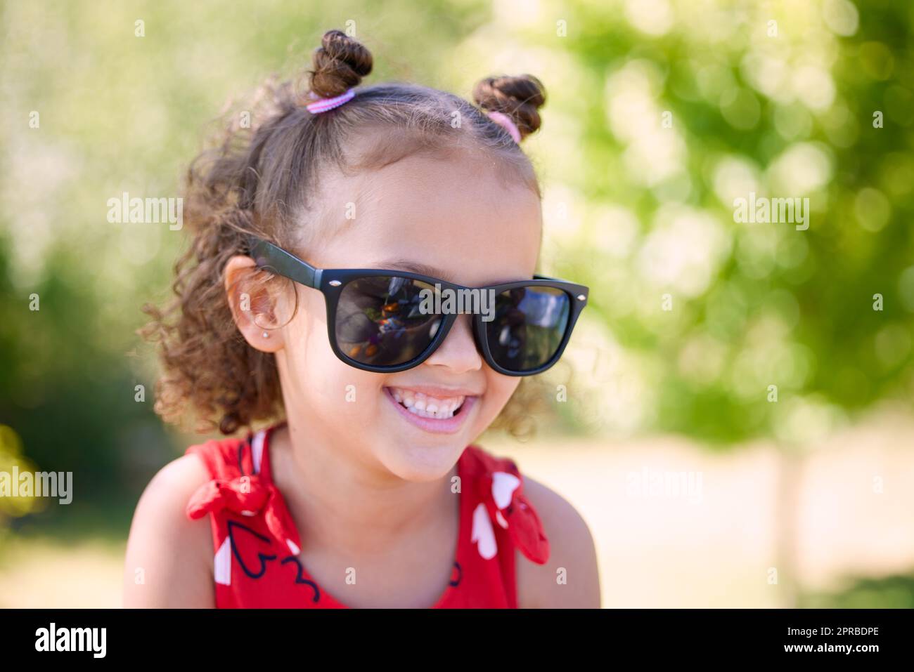 All a girl really needs is a little sunshine. an adorable little girl wearing sunglasses while at the park. Stock Photo