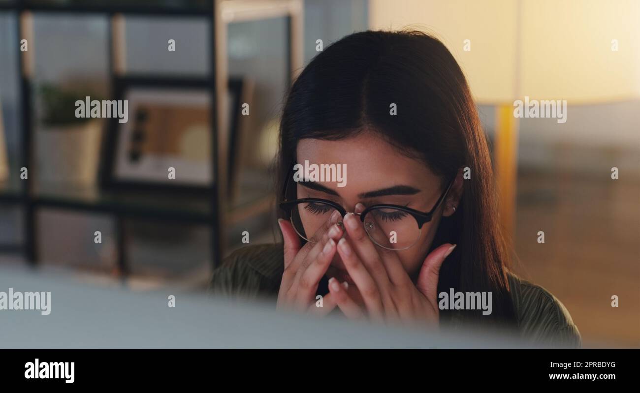 Staring at this screen is really hurting my eyes. a young businesswoman looking stressed out while working on a computer in an office at night. Stock Photo