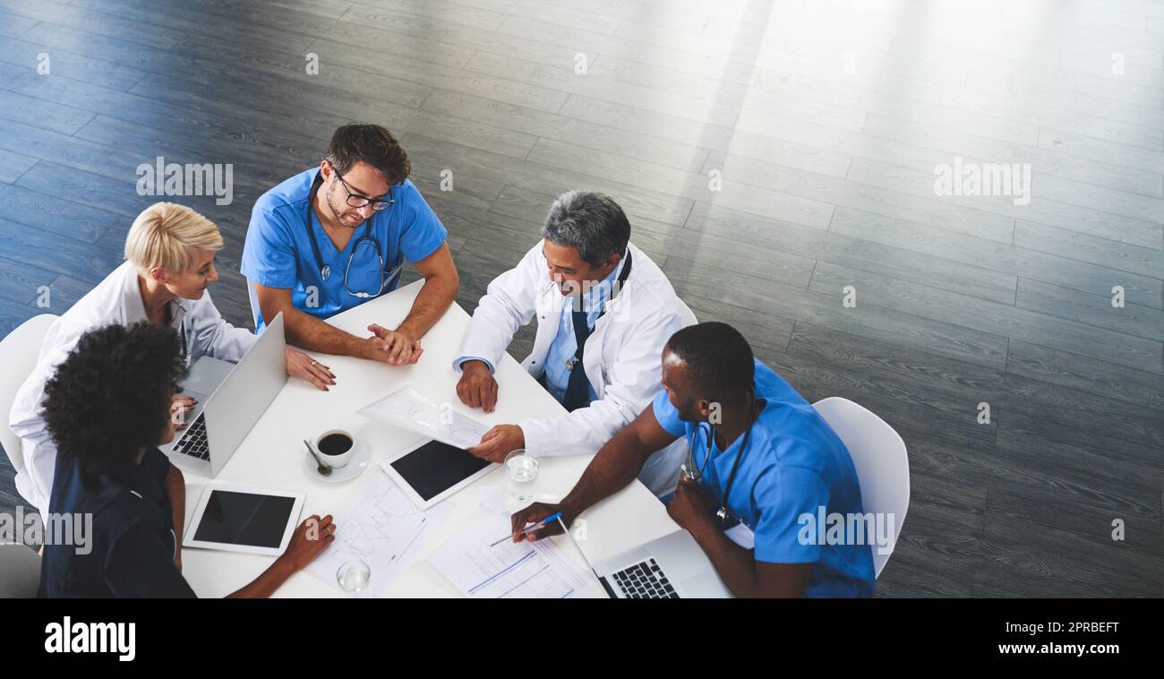 Doctor, nurse and healthcare professional team or group sitting in the boardroom, talking about medicine and discussing treatment during a meeting. Planning and brainstorming a health cure from above Stock Photo
