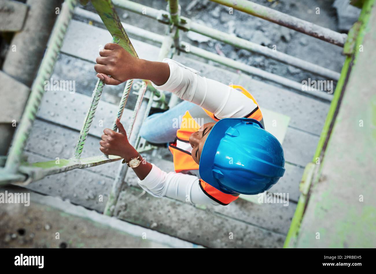 The harder you work the higher you go. a young woman climbing up a ladder at a construction site. Stock Photo
