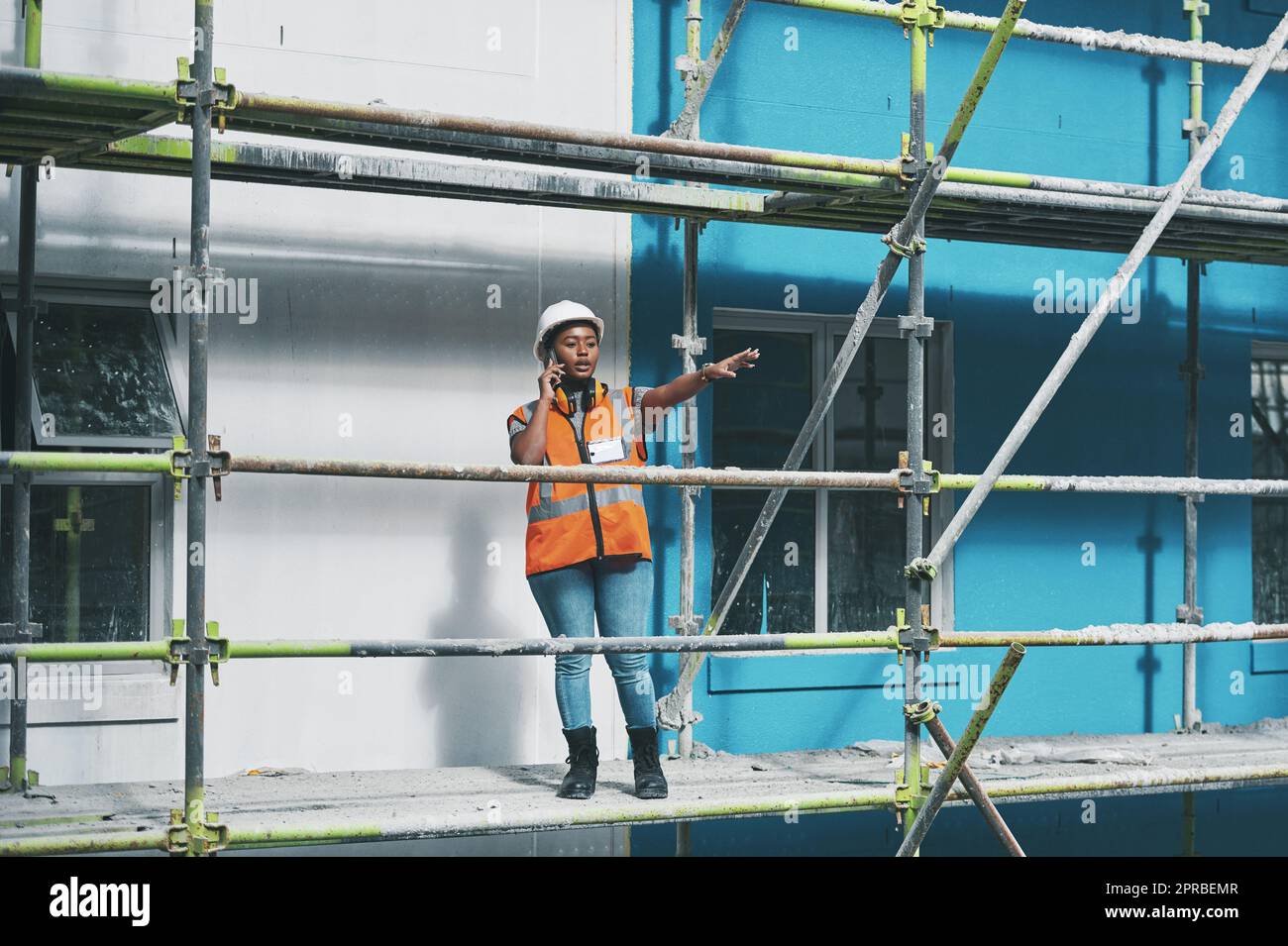 Shes not afraid to delegate and command. a young woman talking on a cellphone while working at a construction site. Stock Photo