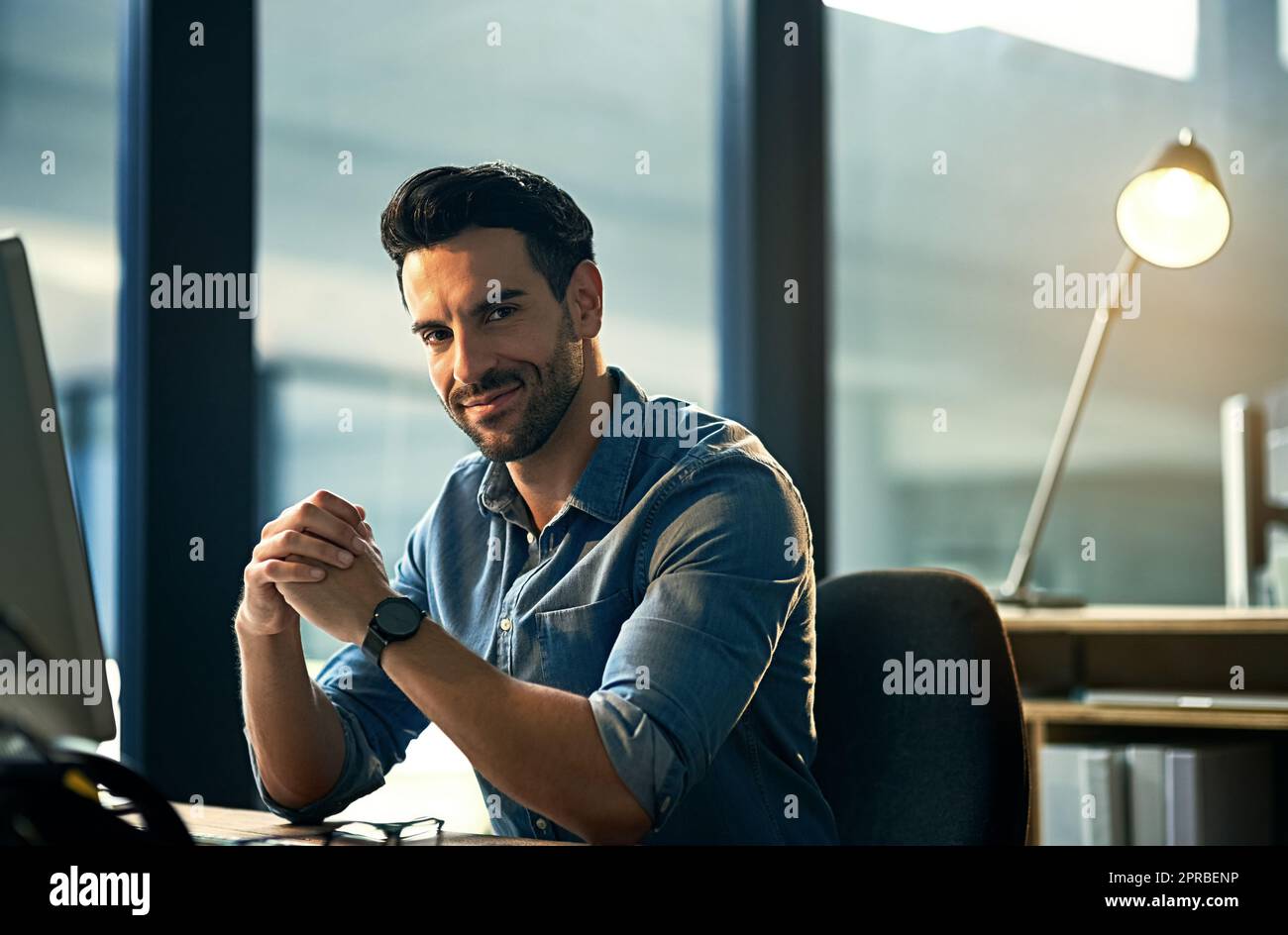 Portrait of a young businessman on a computer during a late night at work. Confident hardworking man at a corporate office desk working overtime, dedicated and committed alone at the workplace. Stock Photo