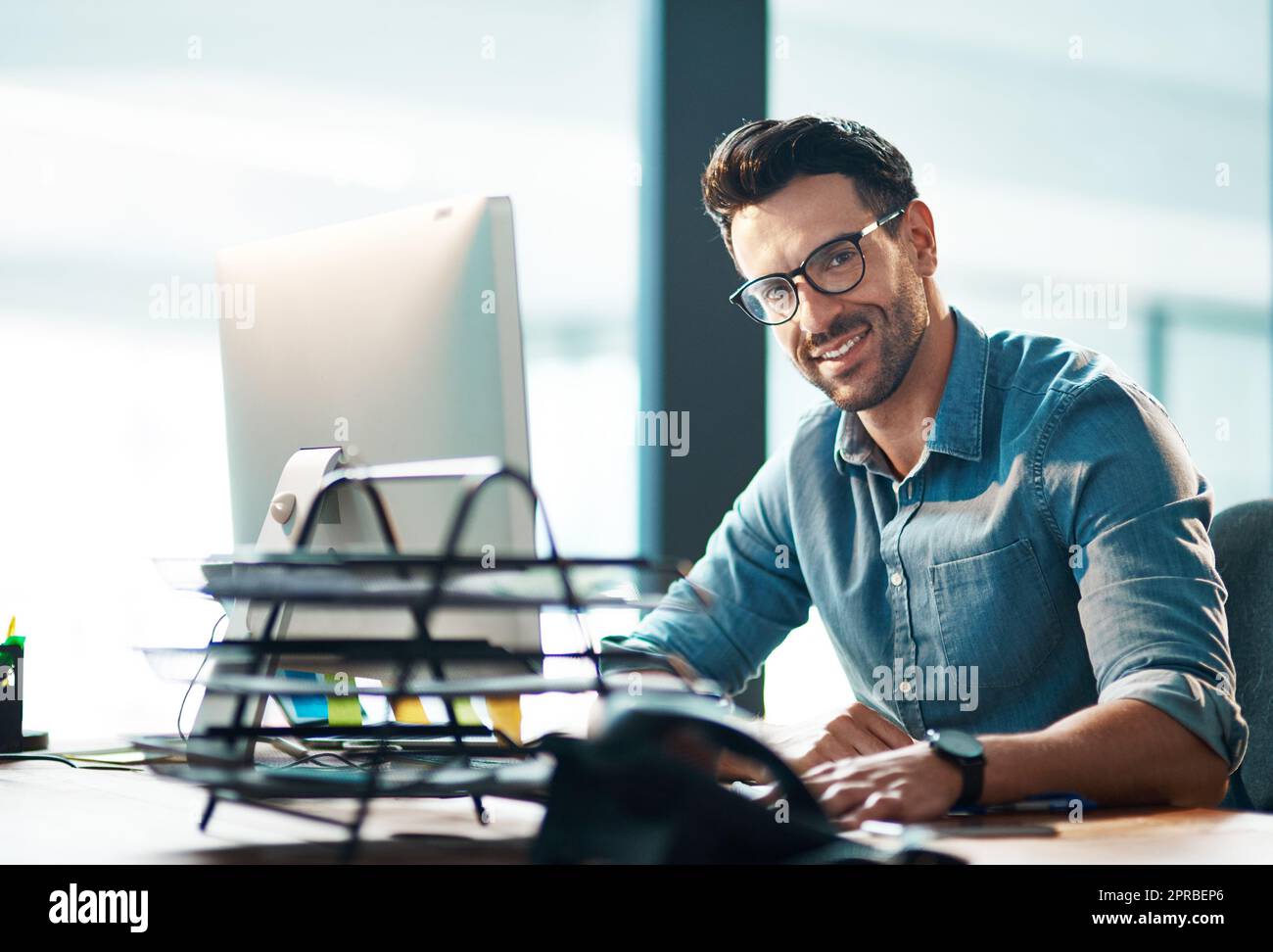 Confident, relaxed and happy professional manager or HR assistant working on a computer in a modern office. Smiling, proud male typing and responding to emails, booking and managing appointments Stock Photo