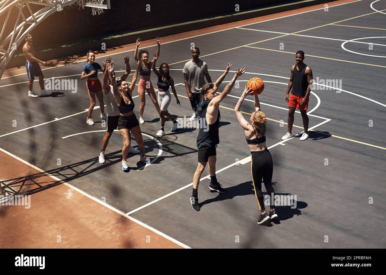 Everyone is totally immersed in the game. a group of sporty young people playing basketball on a sports court. Stock Photo