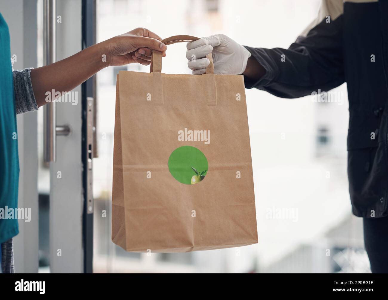 Save yourself the risk of eating out. an unrecognisable man wearing gloves while delivering takeout to a customer at home. Stock Photo