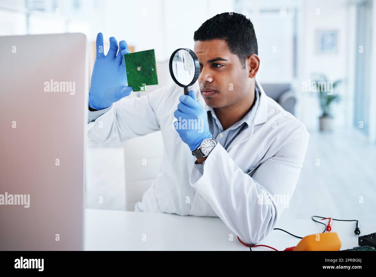 The most respected technician in the field. a young man using a magnifying glass while repairing computer hardware in a laboratory. Stock Photo