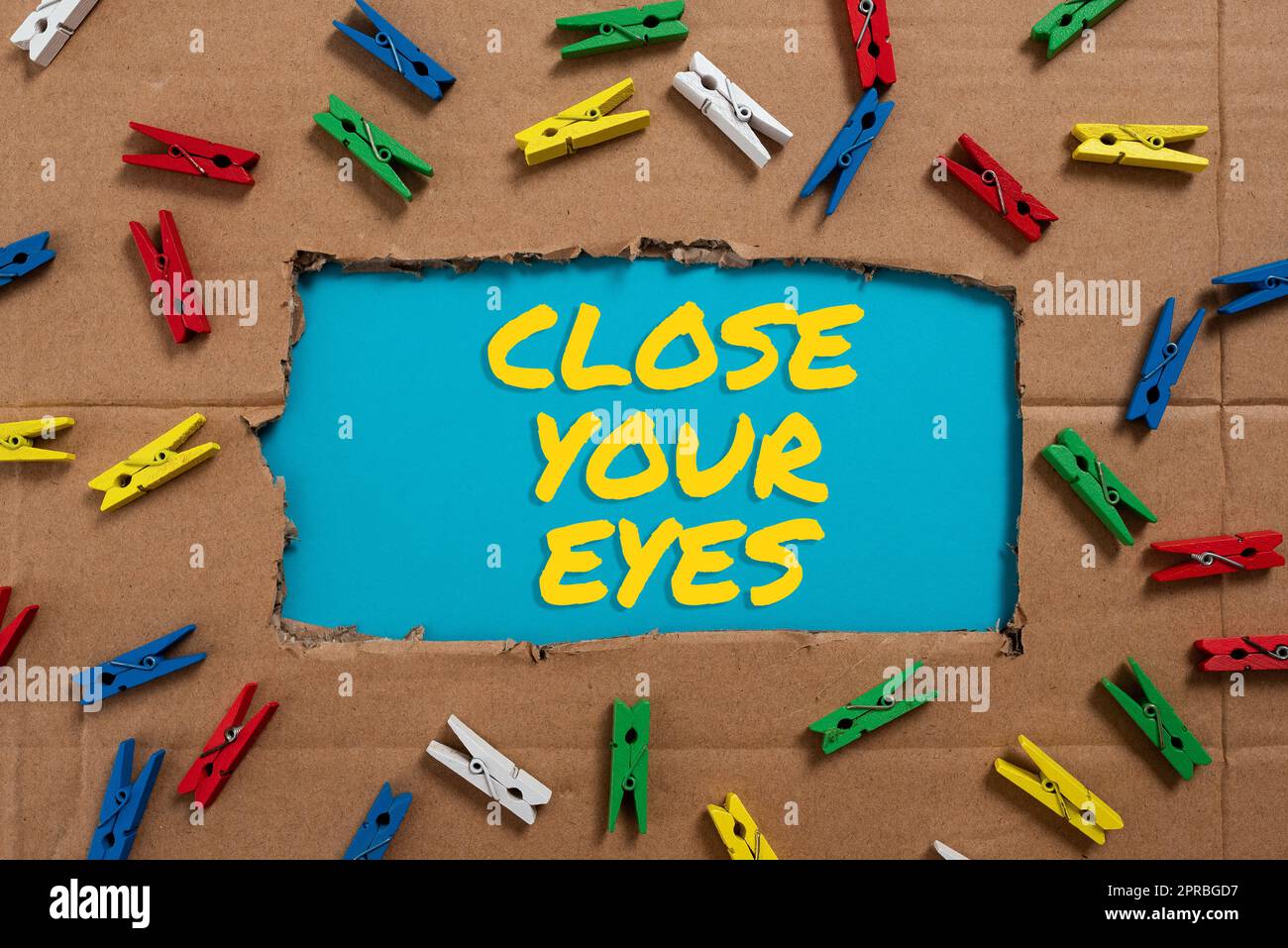 Sign displaying Close Your Eyes. Business overview Cover your sight we have a surprise for you do not peek Important Ideas Written Under Ripped Cardboard With Colored Pegs Around. Stock Photo