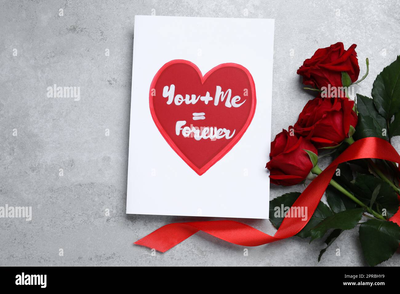 Card with love message near red roses on grey table, flat lay ...
