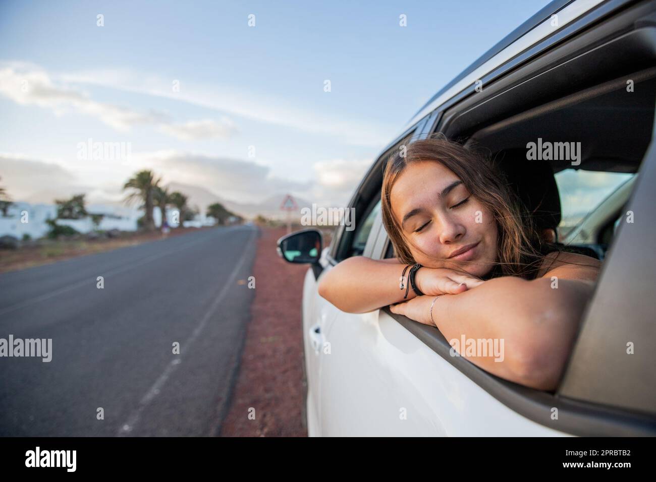 A teenage girl relaxes while in the car and sticks her face out the