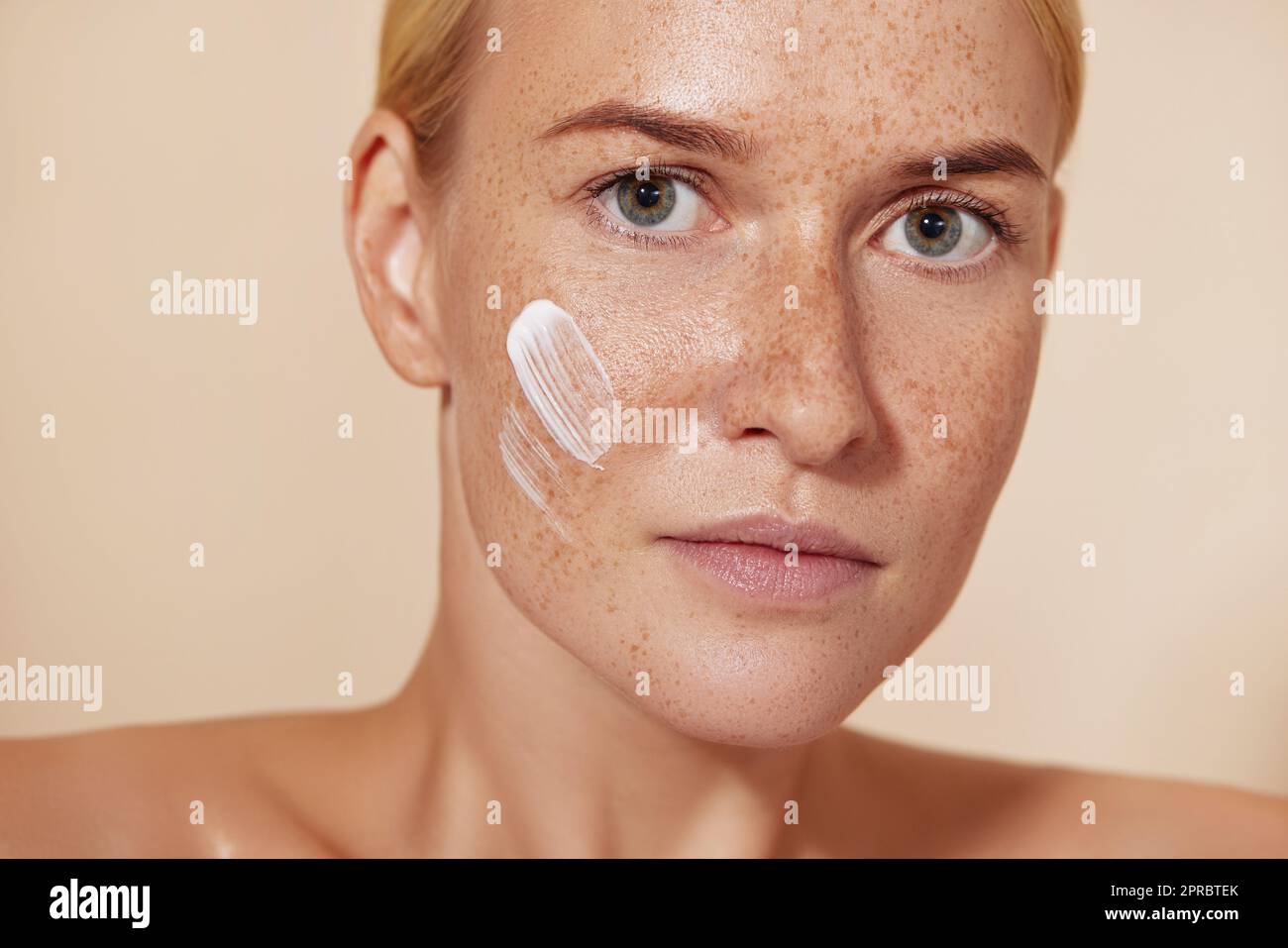 Close up portrait of a woman with perfect smooth skin. Female with freckled skin and cream on a cheek. Stock Photo