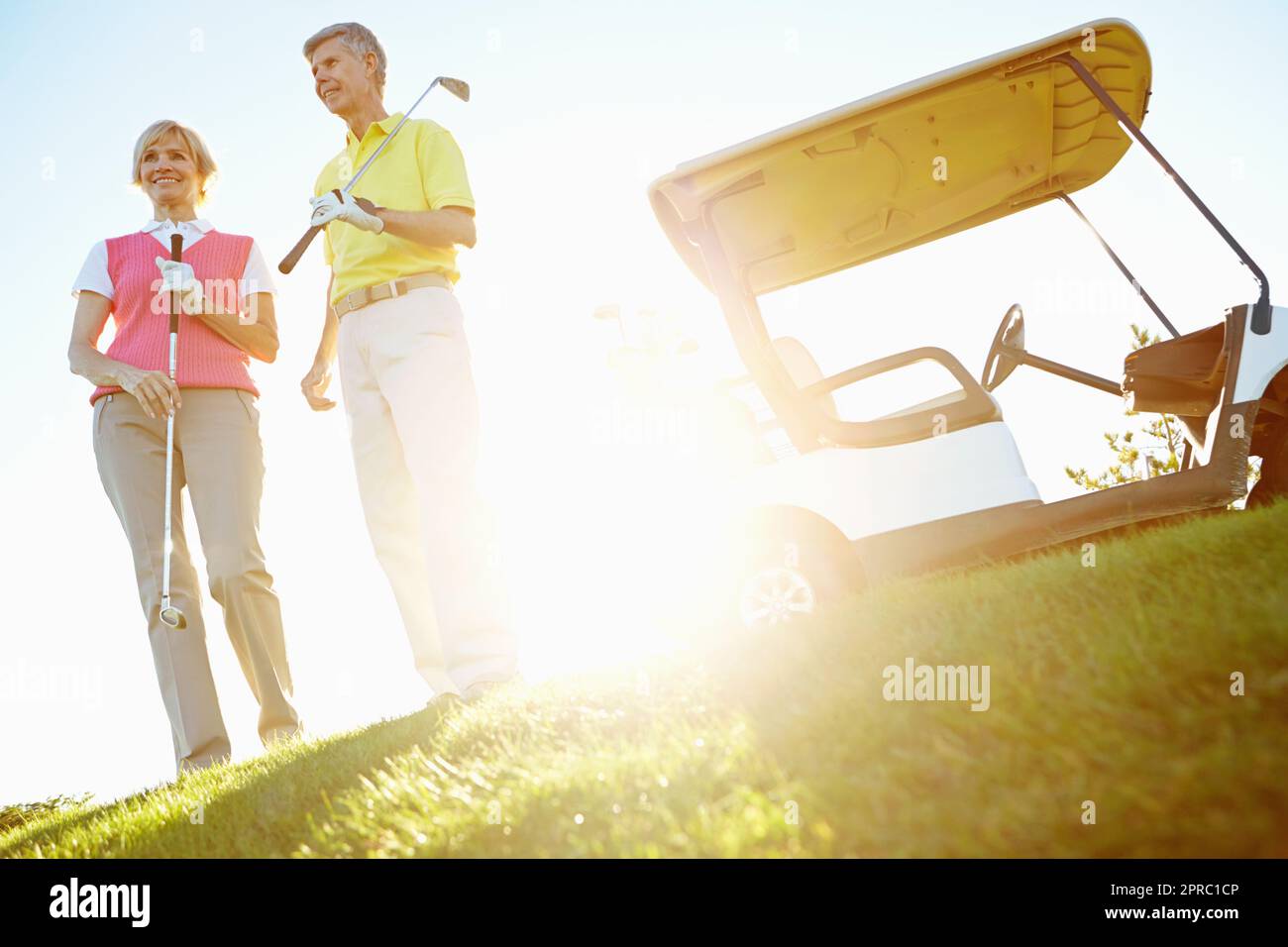 Contentment after a great game of golf. Attractive elderly couple on the green with the sun setting behind them. Stock Photo