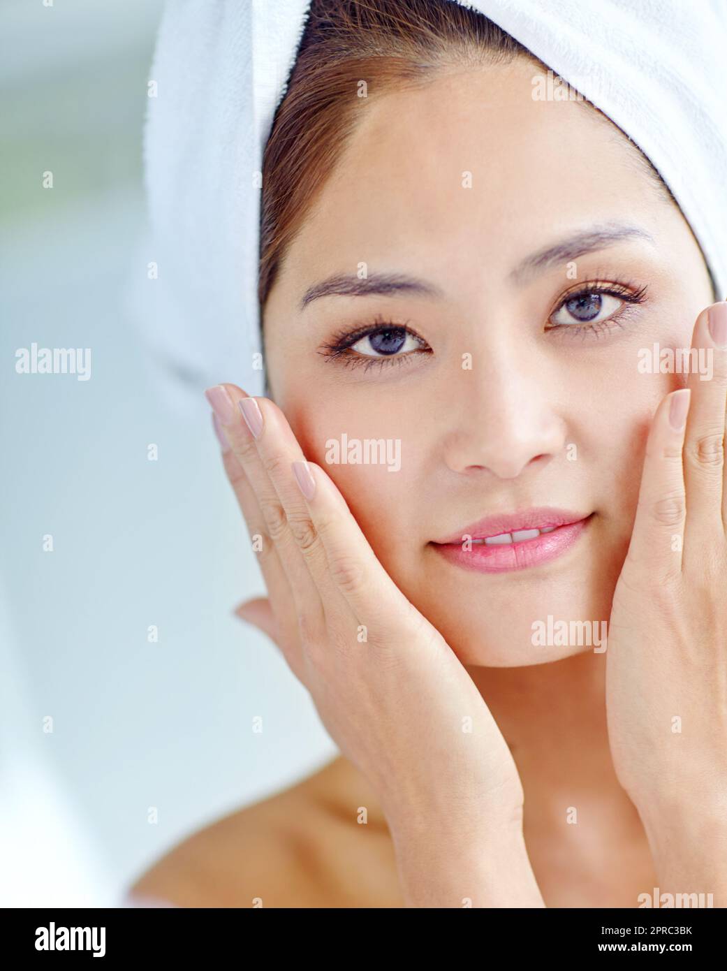 Freshly-showered radiance. A beautiful young Asian woman touching cheeks while wearing a towel on her hand. Stock Photo