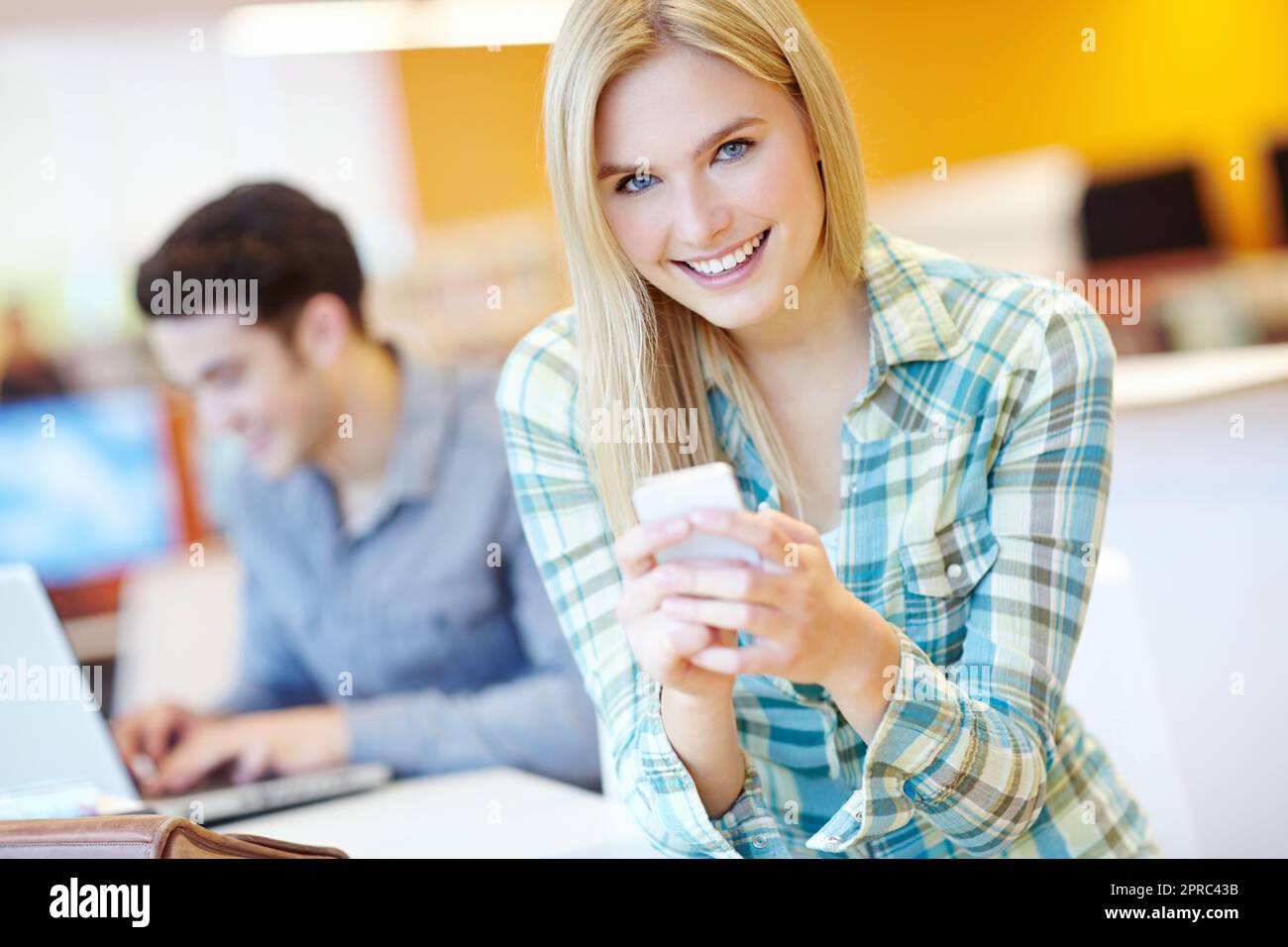 She just heard some juicy gossip. Attractive female student reading a text with her study buddy in the background. Stock Photo