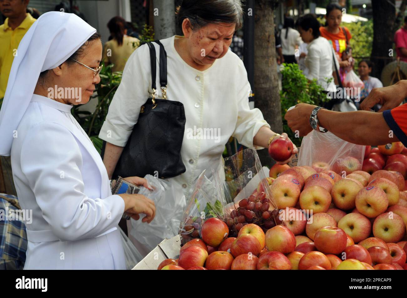 A Catholic nun buying apples at the Soi Prachum market by Silom Road in Bangkok, Thailand. Stock Photo