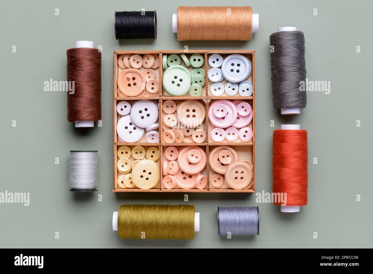 Composition with box of different buttons and thread spools on grey background Stock Photo