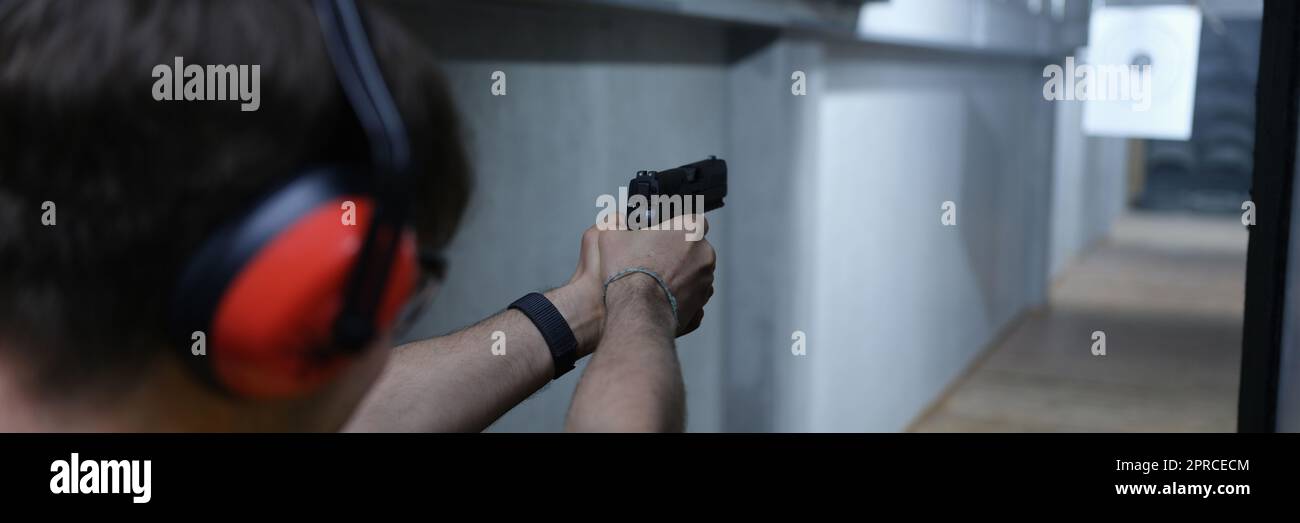 Guy in tactical headphones aiming pistol at target in shooting range