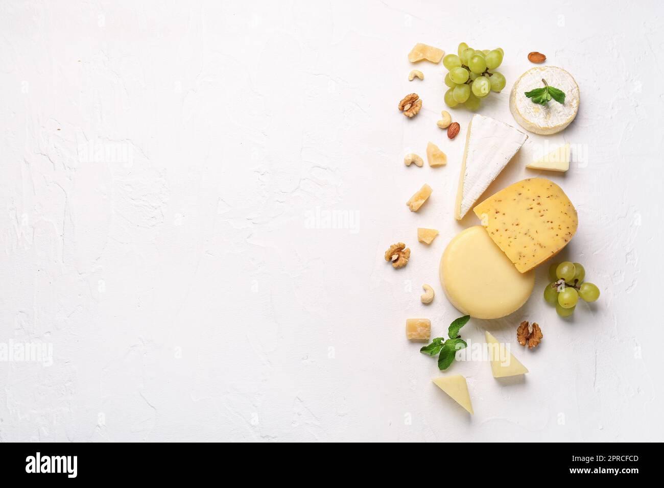 Different types of tasty cheese, nuts and grapes on light background