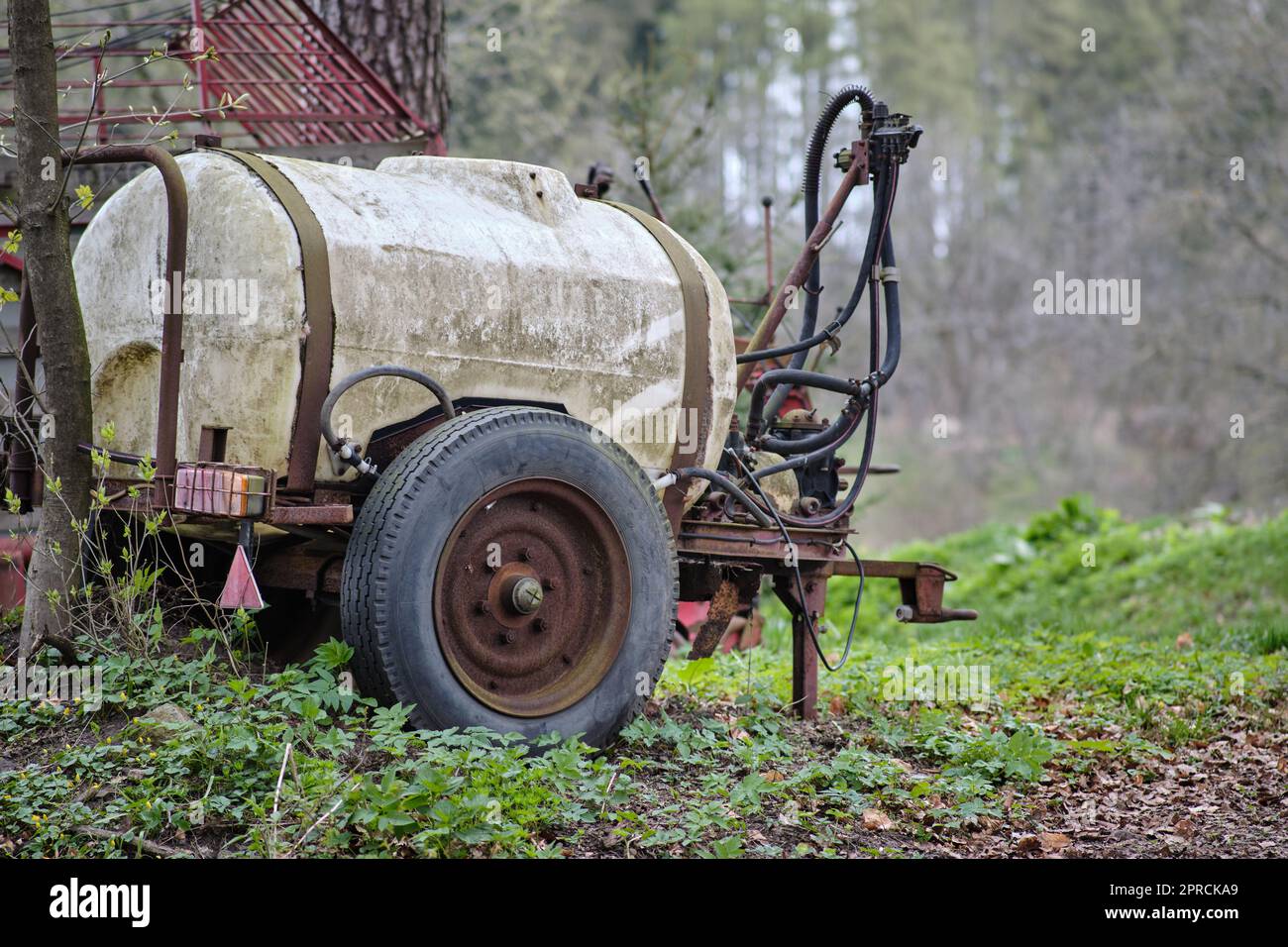 Small vintage agricultural plastic tank for water or artificial fertilizers parked in woodlands. Rusty wheels witness its age. Stock Photo