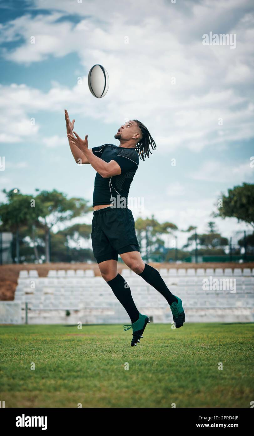 The ball is his to have. Full length shot of a handsome young rugby player catching a ball mid-air on the field. Stock Photo