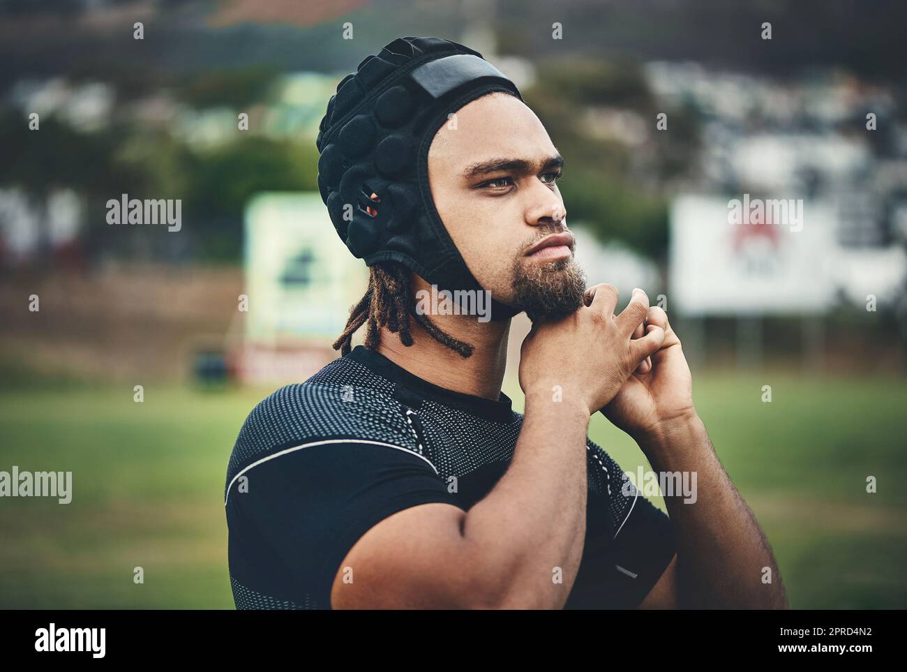 Getting ready to tackle the game ahead. a handsome young rugby player adjusting his headgear while standing on the field during the day. Stock Photo