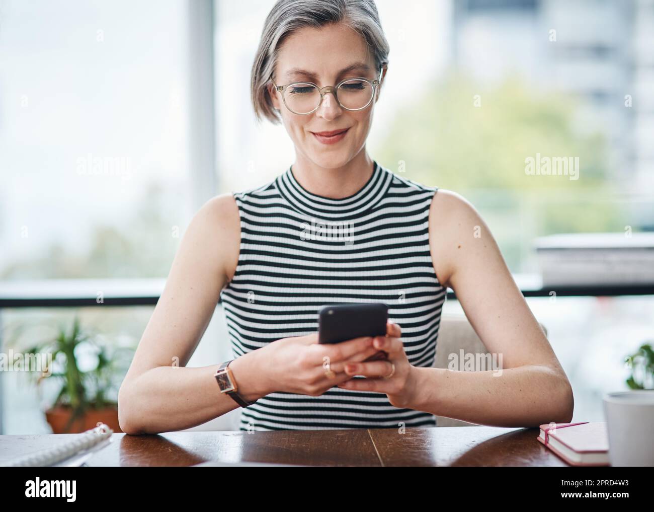 Social media helped me to be even more successful. a mature businesswoman using her cellphone while sitting at her desk. Stock Photo