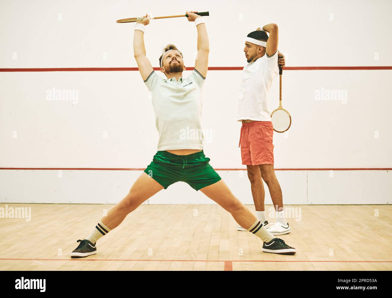Nothing maximises your performance like a good warmup. two young men stretching before playing a game of squash. Stock Photo