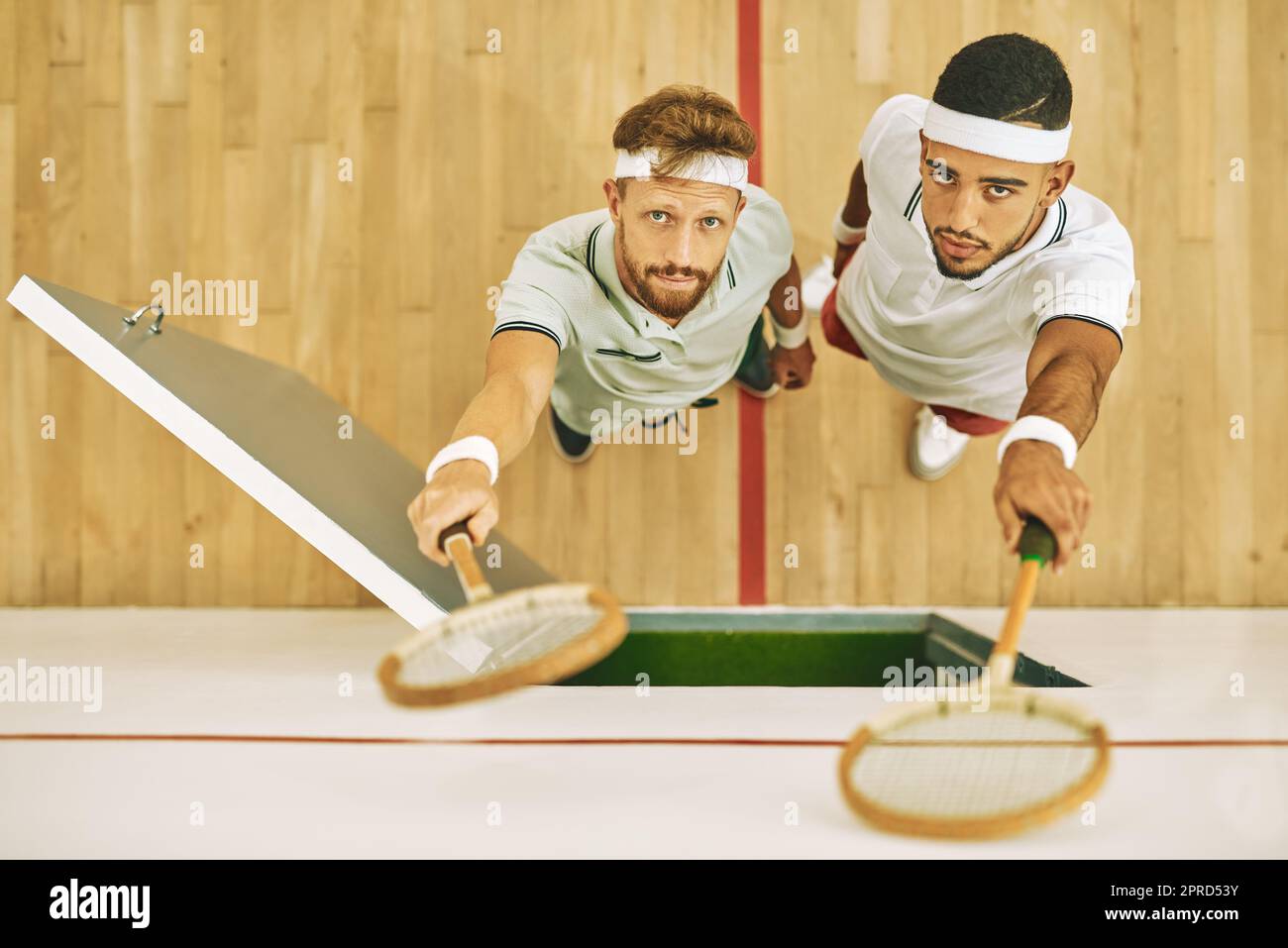 No matter the outcome carry yourself with confidence. High angle shot of two young men holding up their rackets at a squash court. Stock Photo