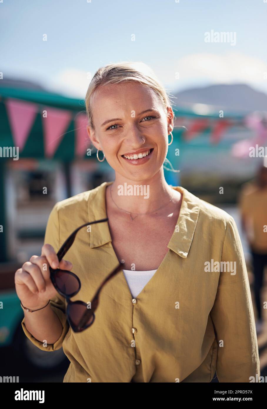 Do you recognise me now. Portrait of a cheerful young woman smiling brightly while standing outside on a beach promenade during the day. Stock Photo