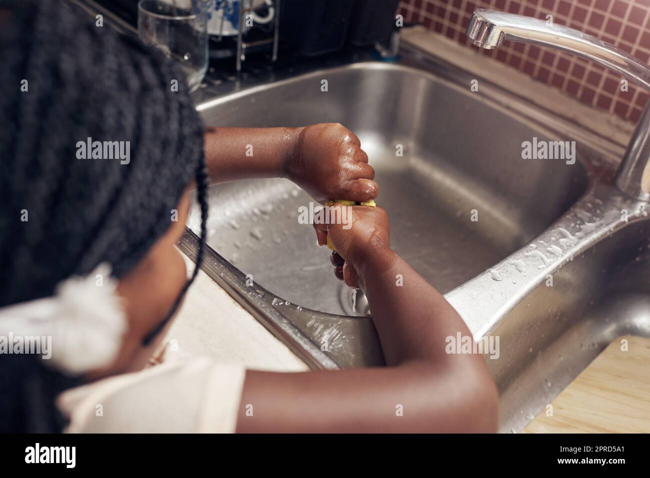 Shes always does her chores. an adorable little girl doing the dishes in the kitchen at home. Stock Photo