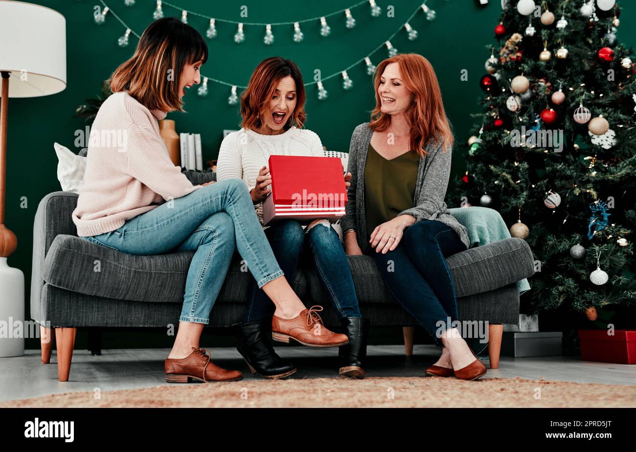 This is amazing. three attractive middle aged women opening presents together while being seated on a sofa during Christmas time. Stock Photo