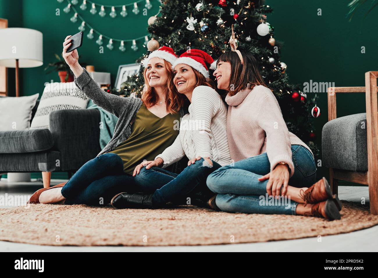 Is everyone in for the photo. three attractive middle aged women taking self portraits together with a cellphone at home during Christmas time. Stock Photo