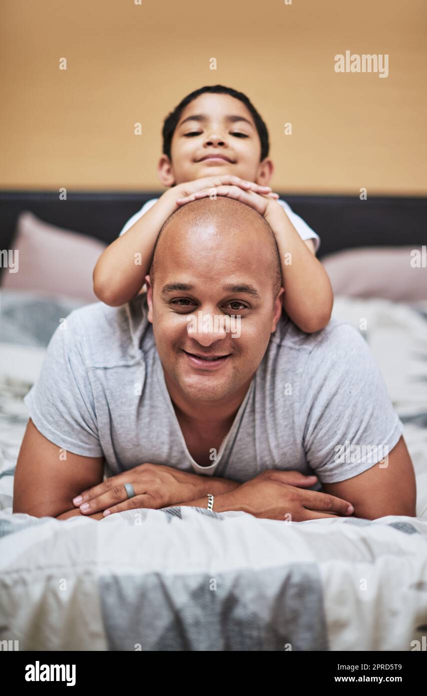 Theres something on my head. Portrait of a cheerful little boy hanging on his fathers back while hanging out in the bedroom at home during the day. Stock Photo