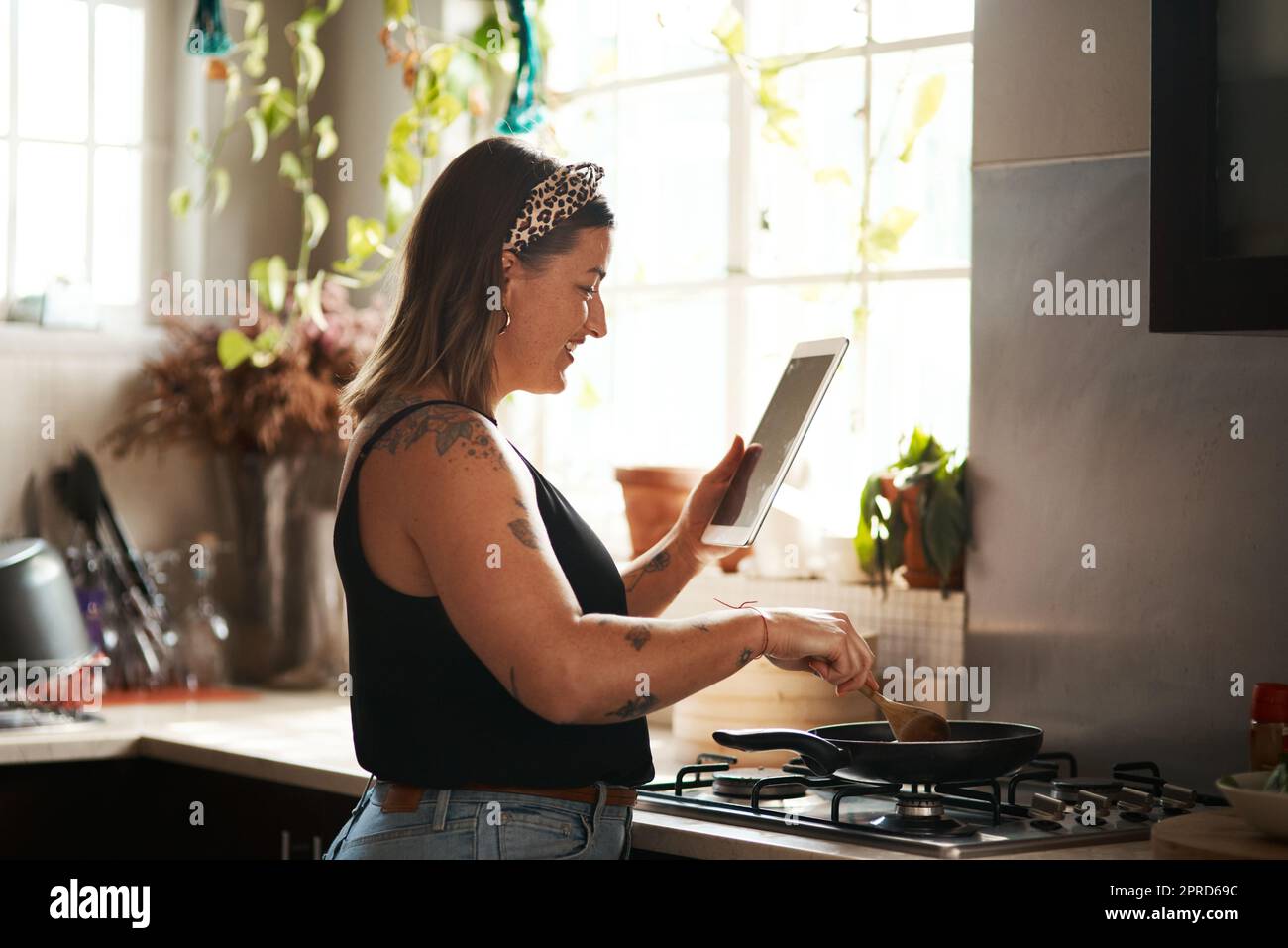 Technology is an awesome cooking tool. a young woman using a digital tablet while preparing a meal at home. Stock Photo