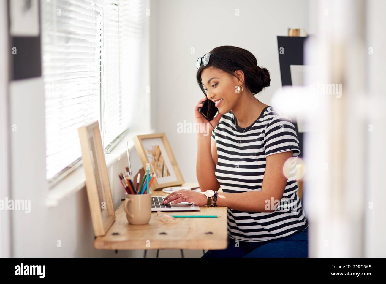 Everyone is calling in to order my work today. an attractive young artist using a laptop and making a phone call inside her studio at home. Stock Photo
