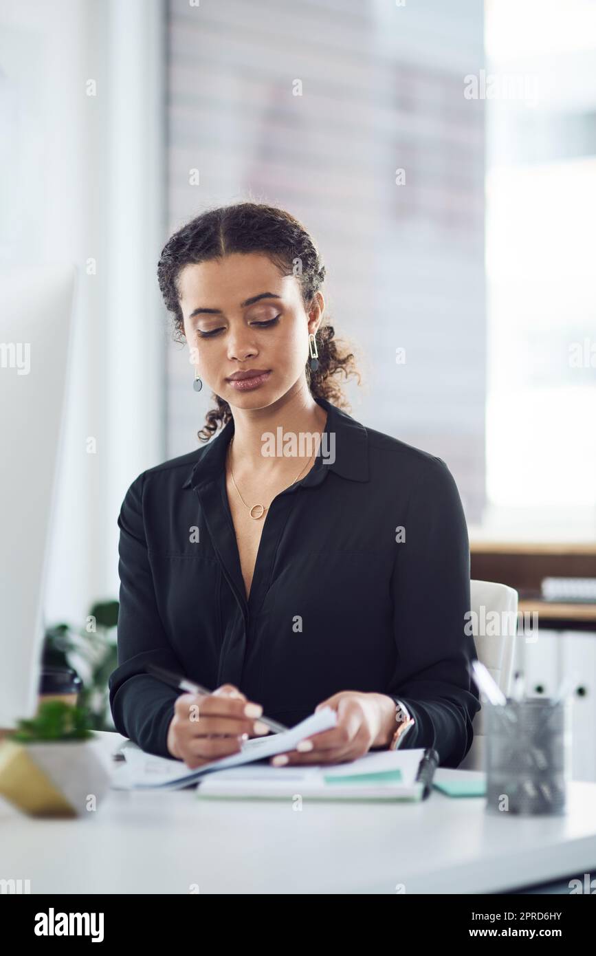 All plans need her approval first. a young businesswoman going through paperwork in an office. Stock Photo