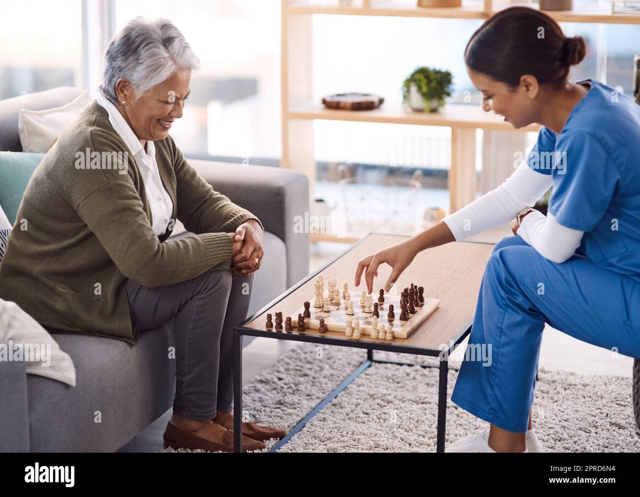 Playing games are a great way to keep the mind active. a young nurse playing chess with a senior woman in a retirement home. Stock Photo