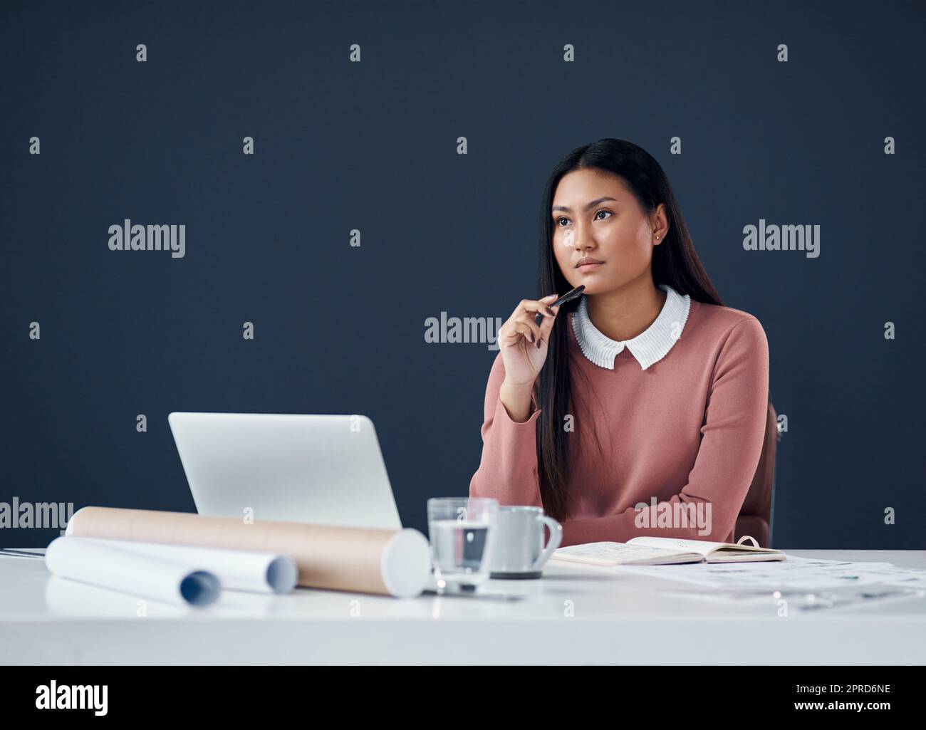 Shes got a mindful of ideas. an attractive young female architect looking thoughtful while working on a laptop in her office. Stock Photo