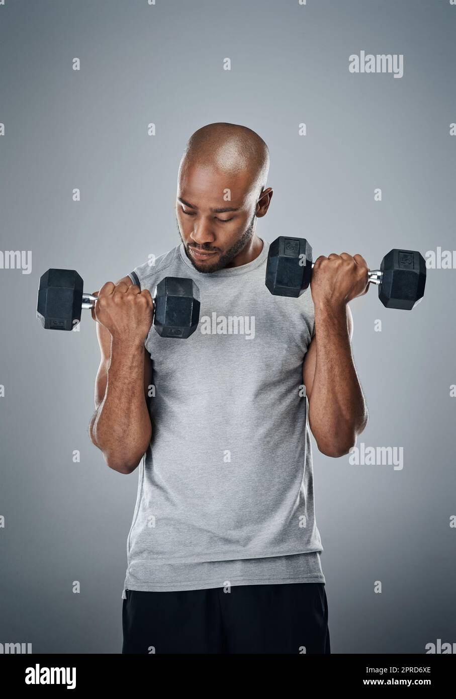 Work on a stronger and you. a sporty young man working out with weights against a grey background. Stock Photo