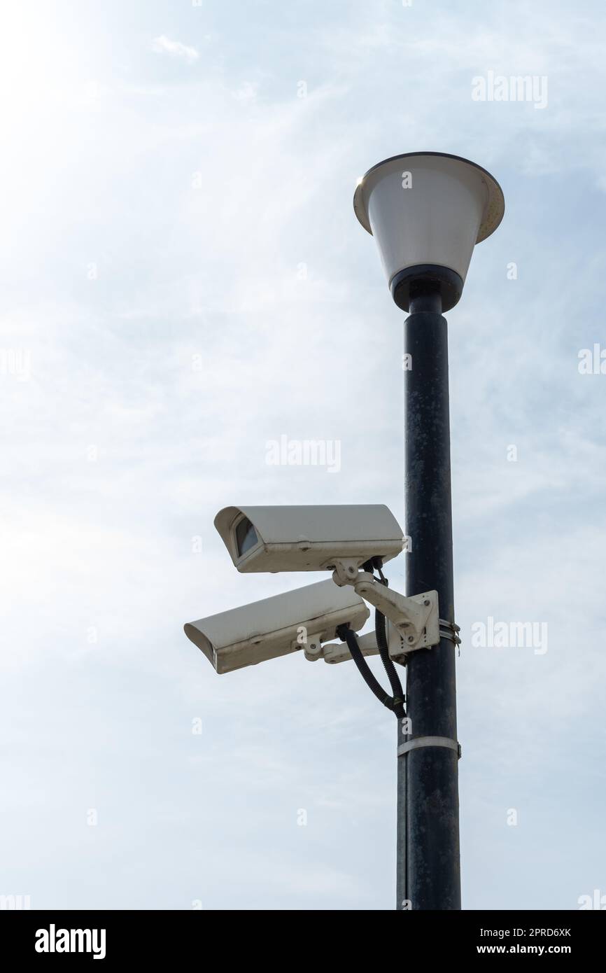 Surveillance cameras mounted on a lamp post against a blue sky