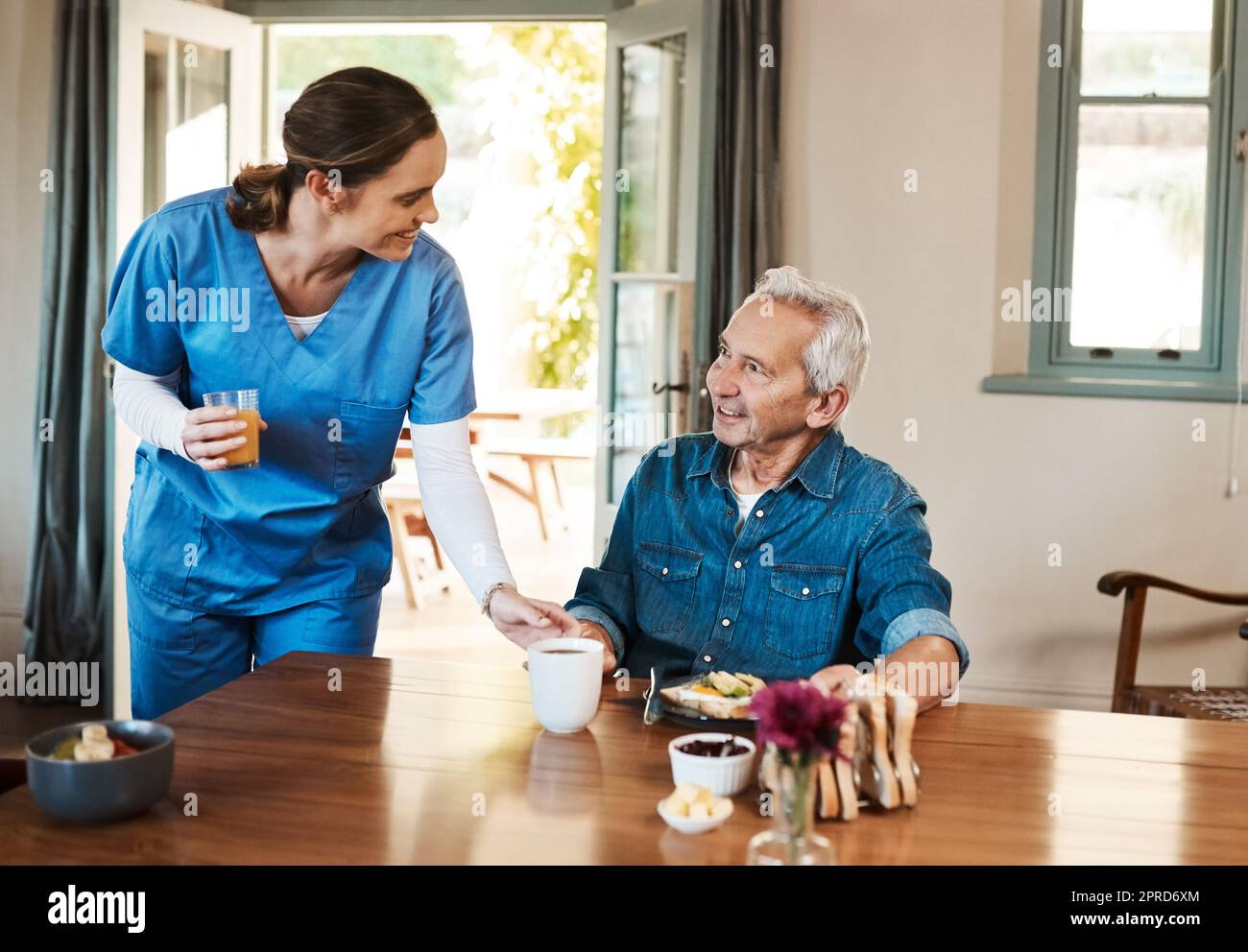 Can I get you anything else. a young nurse checking up on a senior man during breakfast at a nursing home. Stock Photo