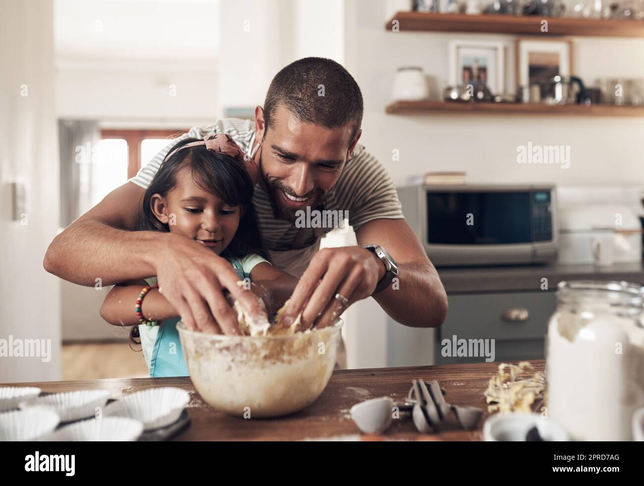 The world, wed discovered, doesnt love you like your family loves you. a father teaching his daughter how to bake in the kitchen at home. Stock Photo