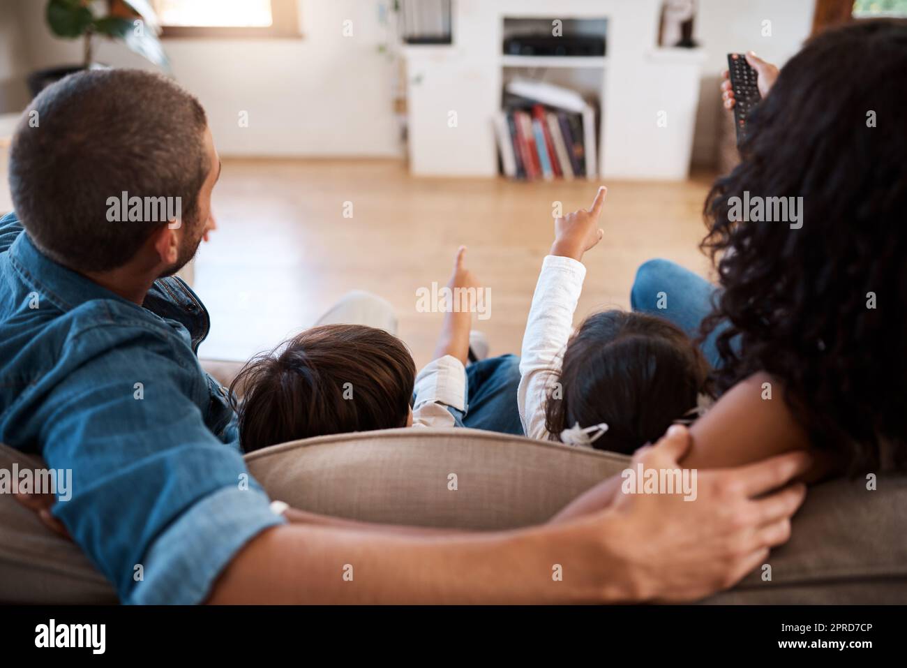The kids always get to chose what to watch. Rearview shot of a couple watching something on the television with their two young kids. Stock Photo
