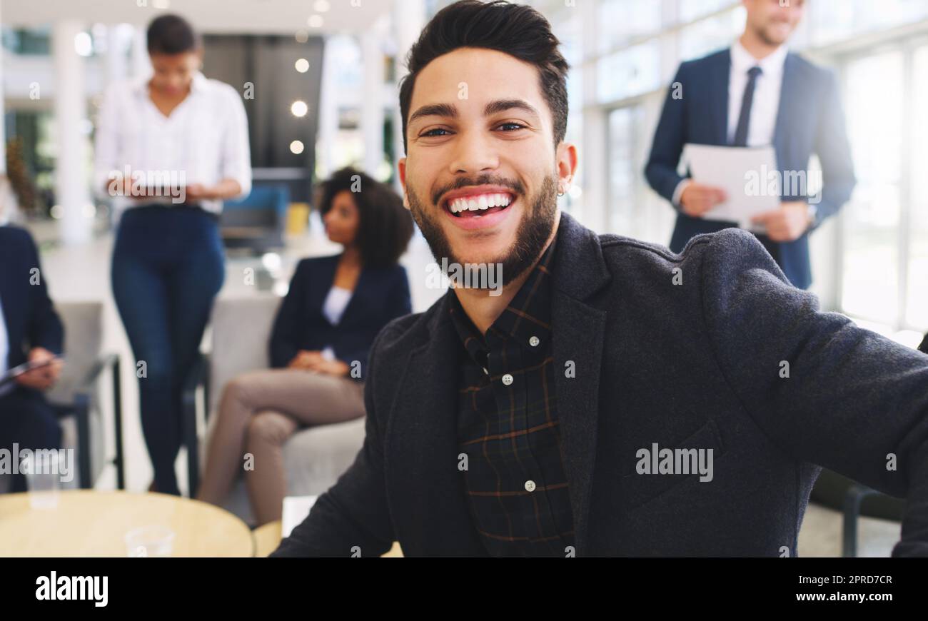 I smile my way through challenges. Cropped portrait of a handsome young businessman sitting and smiling while his colleagues work behind him in the office. Stock Photo