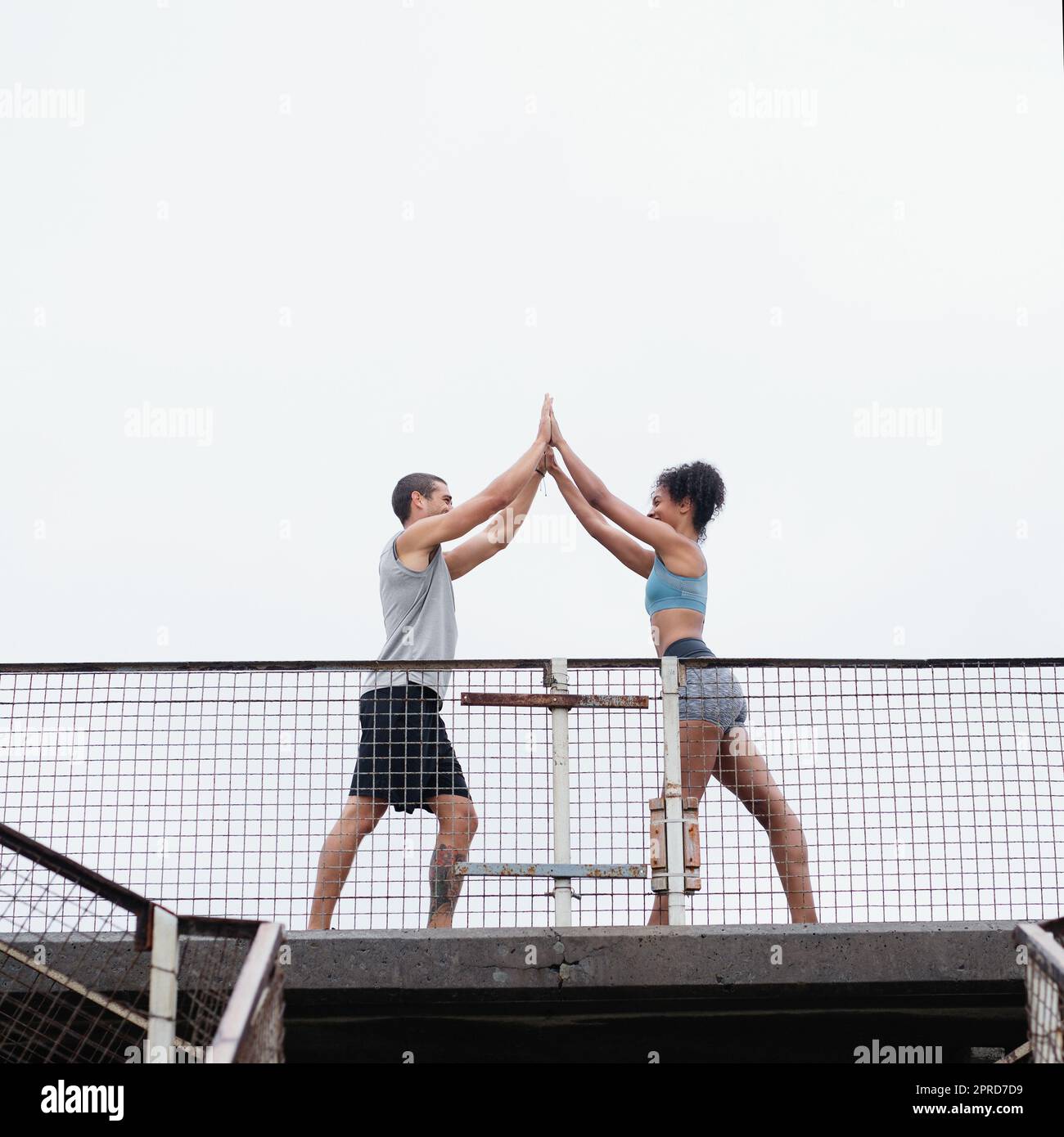 We always achieve new feats together. Full length shot of a sporty young couple joining for a high five while exercising outdoors. Stock Photo