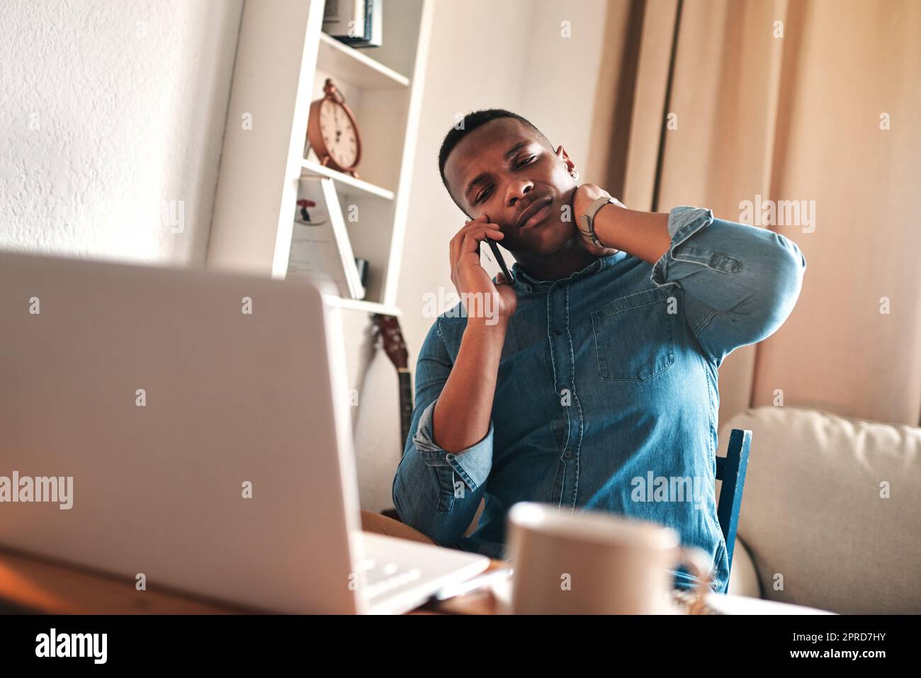 Headache, stress and pain while talking on a phone call and working from a laptop at home. Worried, anxious man rushing to meet a deadline, looking unhappy while suffering from neck pain and tension Stock Photo