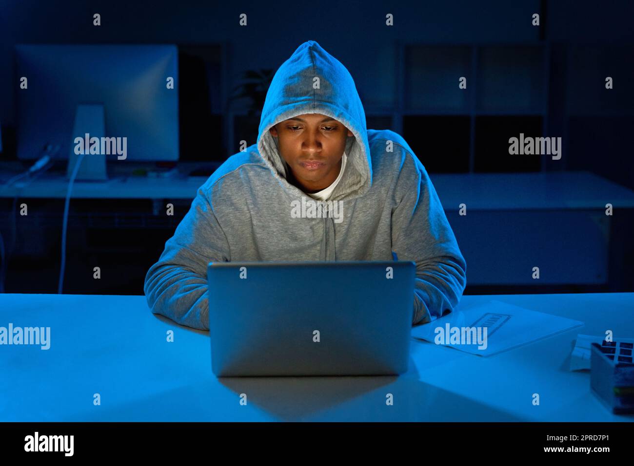 Hacking away in the late hours of the night. a young male hacker using a laptop in the dark. Stock Photo