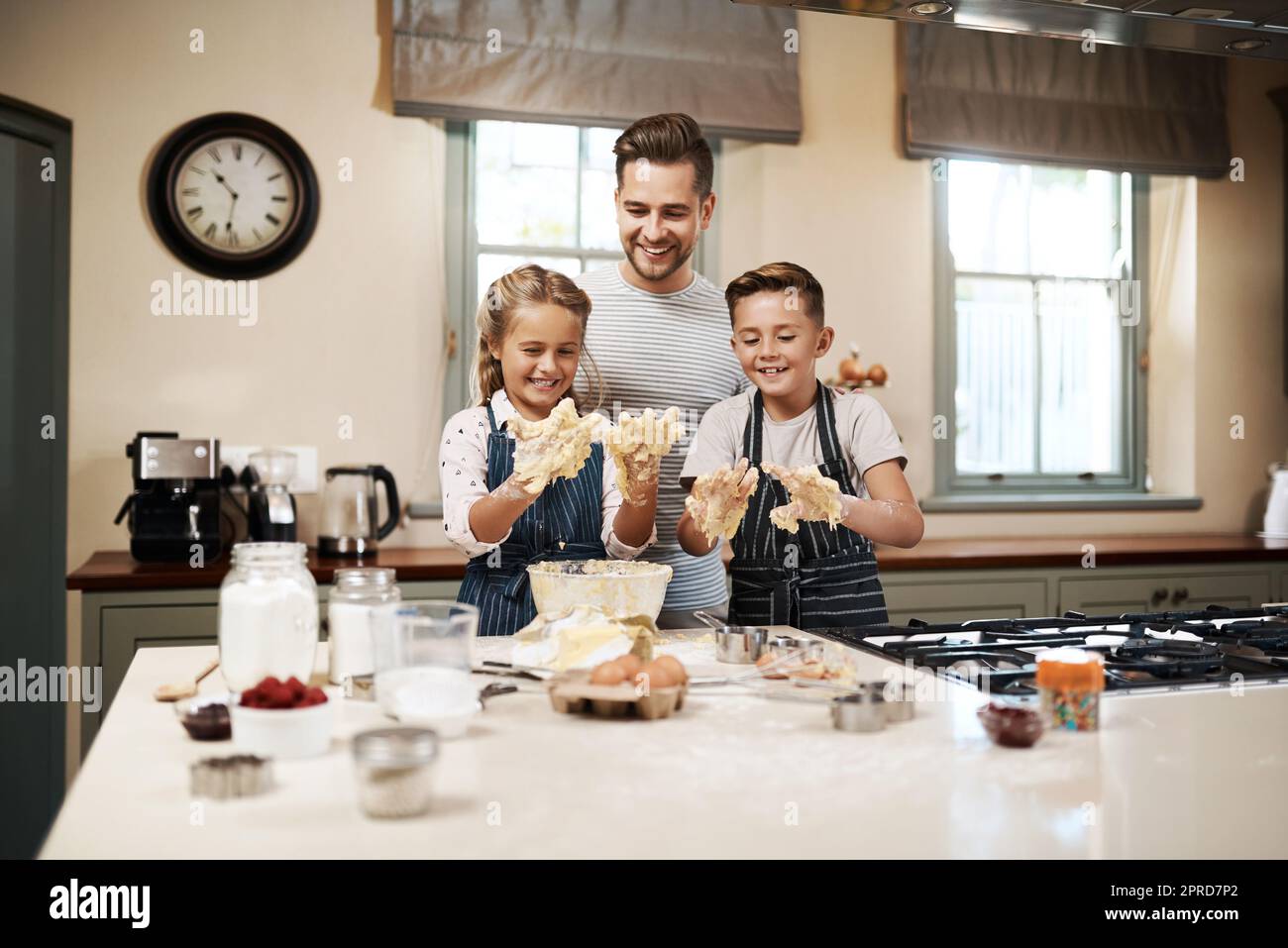 Its always fun when it involves getting your hands dirty. a man and his two children baking in the kitchen at home. Stock Photo