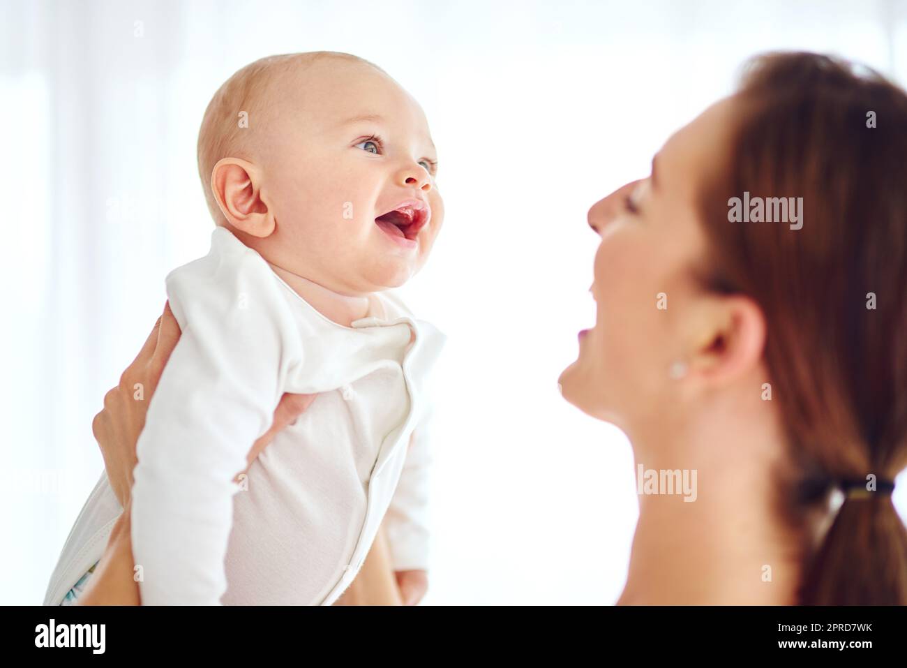 Loving, caring and smiling mother carrying her baby at home bonding. Female embracing motherhood holding her baby in the air enjoying a sweet moment of love, care and happiness in the joy of life. Stock Photo